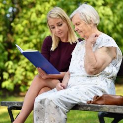 Young,Woman,Reading,A,Book,Elderly,Woman,In,The,Park.